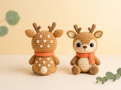 Two handmade crocheted deer toys sitting side by side on a light beige surface against a soft cream background. One deer is shown from the back, and the other is shown from the front, both wearing orange scarves and featuring white spots on their backs.