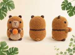 Three views of a crocheted capybara plush toy holding an orange nut, displayed on a light cream background with decorative green leaves in the corners.