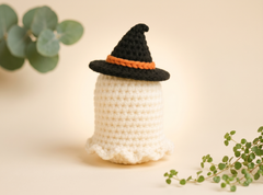 Small white amigurumi ghost with black safety eyes, blush cheeks, a stitched smile and a wavy hem.