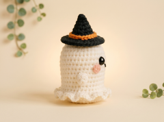 White crochet ghost in a pointed black hat tilted to one side, with tiny stubby arms.