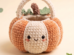 A cute crocheted pumpkin-shaped basket with a smiling face, featuring orange and cream stripes, a cream handle, and a small brown stem with green leaves on top, set against a soft beige background.
