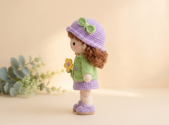 Handmade crochet girl doll wearing a green jacket, lilac skirt, white socks and strap shoes.