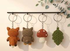Small crocheted fox, owl and toadstool keychains with an acorn below, on a pale background.