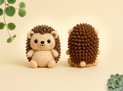 A crocheted hedgehog toy shown from the front and back on a warm cream background, with decorative green leaves in the corners.