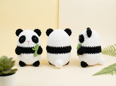 Three crocheted panda toys are displayed on a light beige surface against a cream background. The center panda is shown from the back, while the left and right pandas show the front and side profiles.