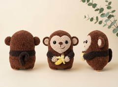 Three crocheted monkey plush toys shown from different angles on a warm beige background, with a decorative eucalyptus branch in the top right corner.